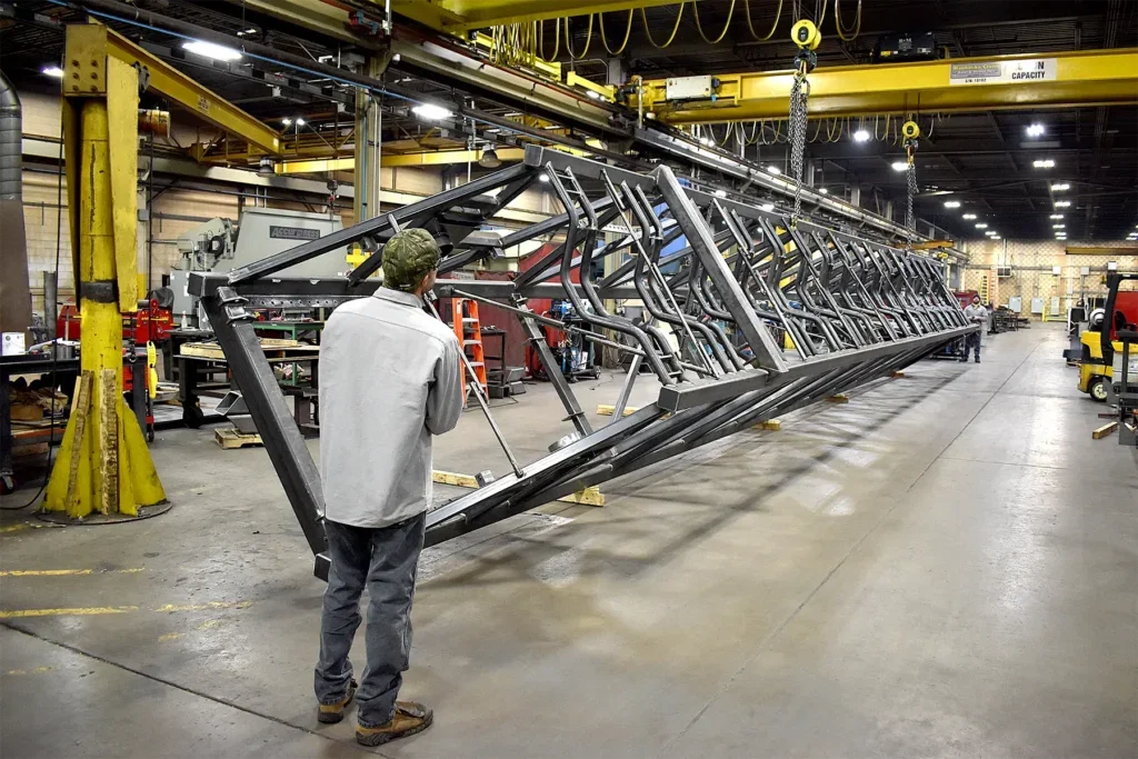 Telescopic conveyor rail rotated by overhead cranes for weld access at Cutting Edge Fabrication.